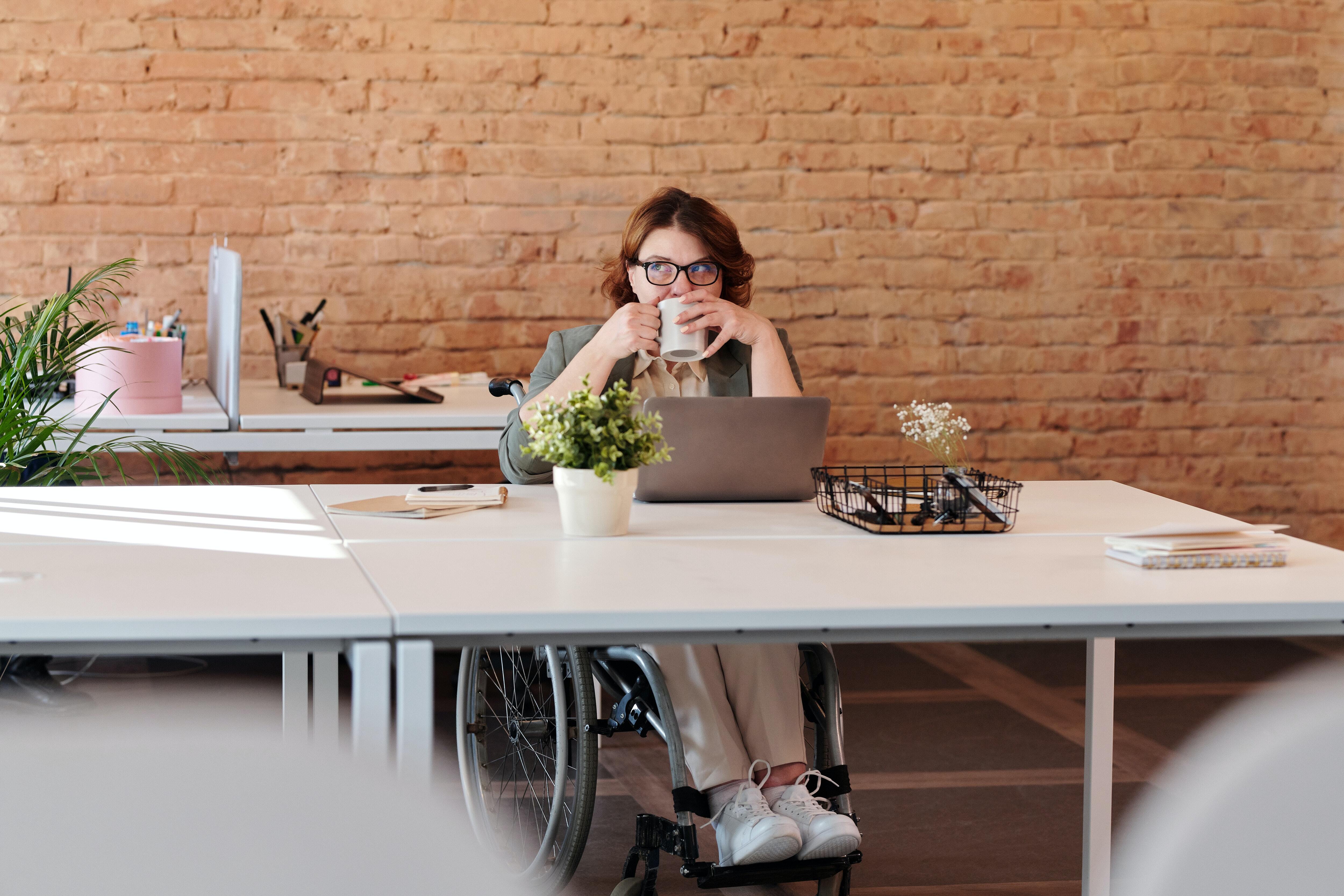 Woman in wheelchair on computer with mug